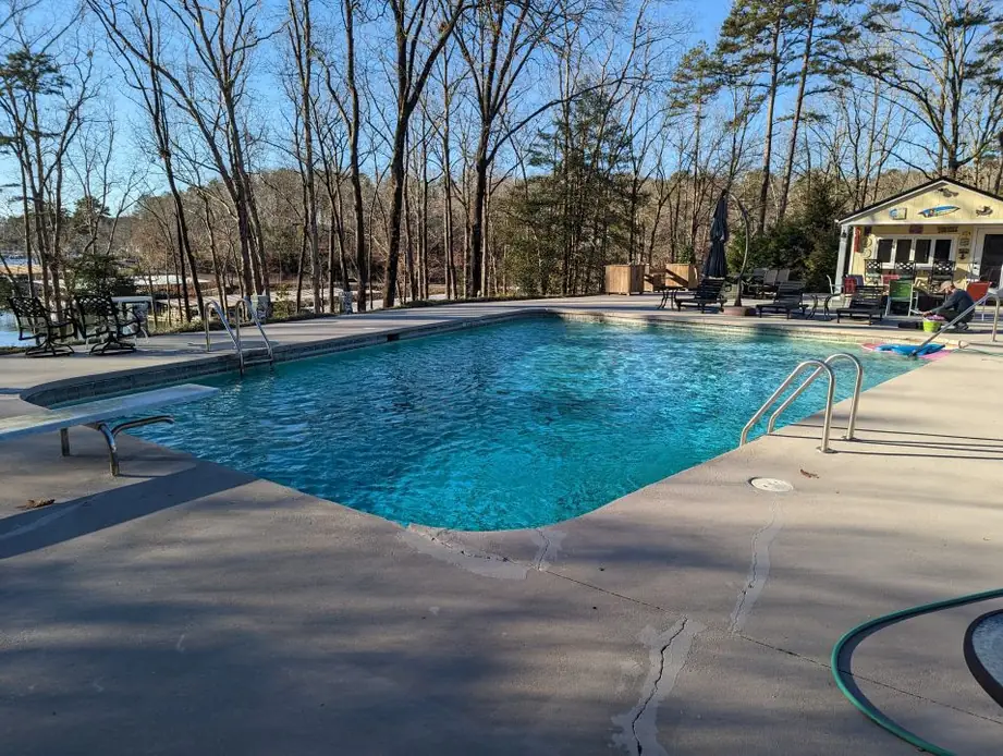 Rectangular in-ground pool with a diving board and a concrete deck, a lake and pool house behind