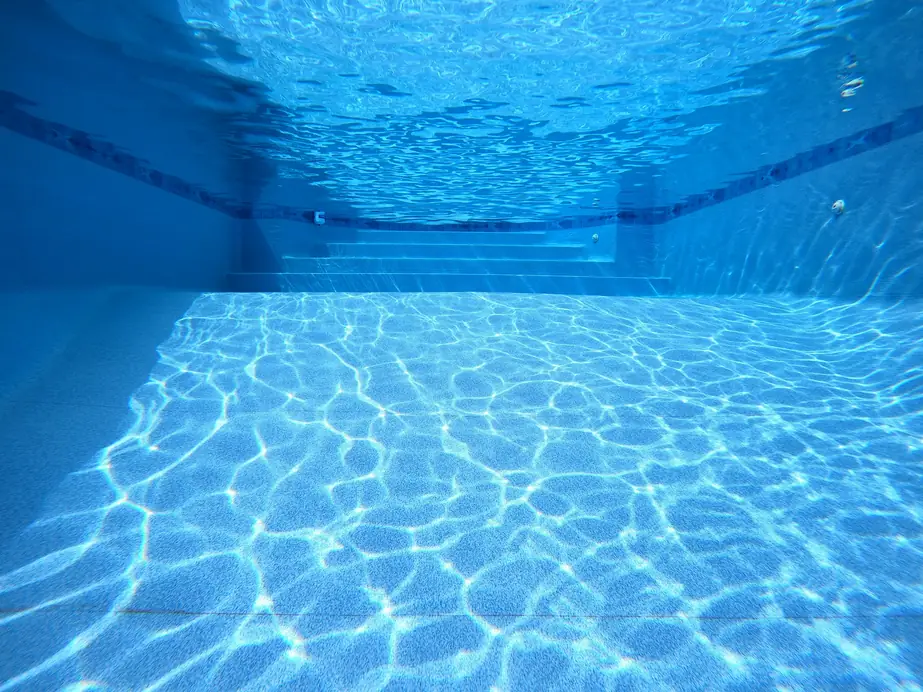 Underwater view along a pool floor toward the steps, sunlight caustics across the plaster